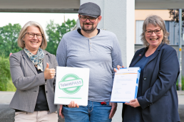 Auf dem Bild sind drei Personen zu sehen. In der Mitte steht Tobias Schumacher von der Pegnitz Gebäudereinigung gGmbH. Links daneben hält Claudia Drechsel die TalentPass Mappe in der Hand. Rechts daneben präsentiert Nina Gillitzer von der Handwerkskammer für Mittelfranken das ValiKom-Zertifikat für Herrn Schumacher.